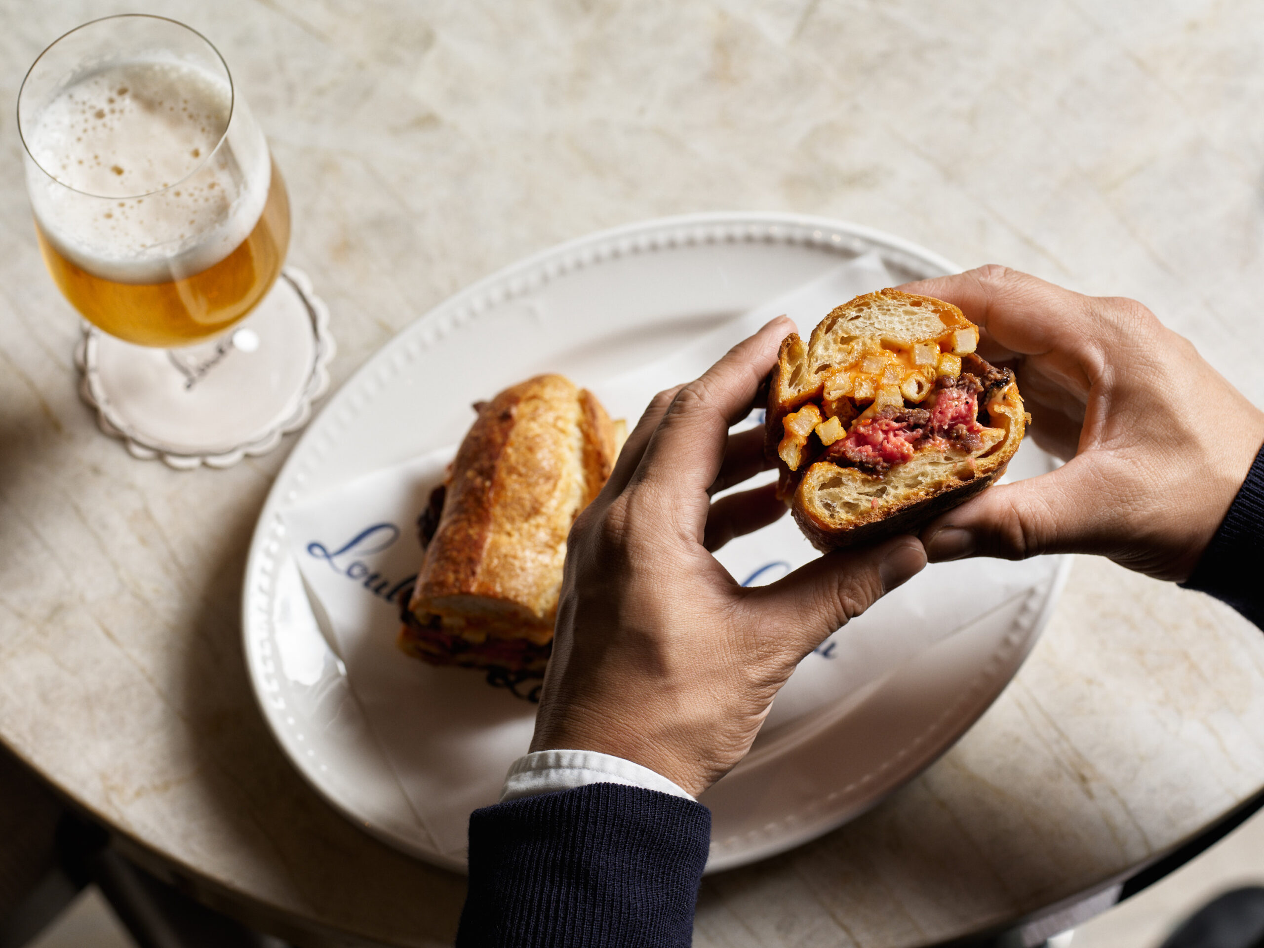 inside of sandwich with beef patty, fries and sauce served next to beer